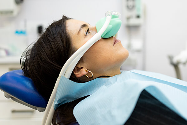 An adult woman sits in a dentist's office wearing a nasal mask to inhale nitrous oxide. Dentist fear concept. Feeling of relaxation with laughing gas. Visit a dentist with relaxation.
